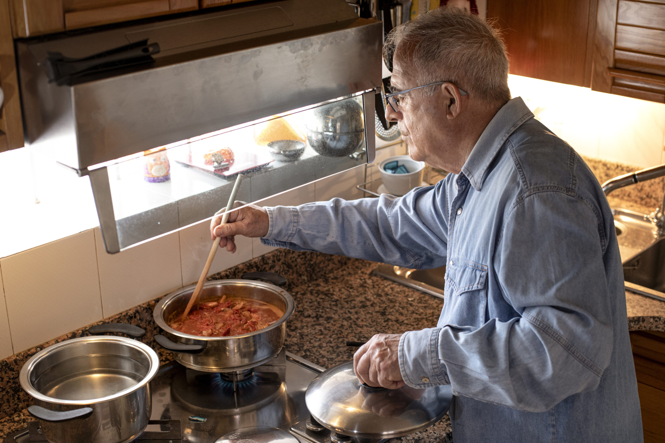Uomo anziano in camicia in jeans prepara il sugo in cucina